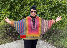 a woman with her arms outstretched wearing a colorful crocheted poncho and black leggings