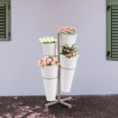 four white flower pots with pink and white flowers in them are on a metal stand