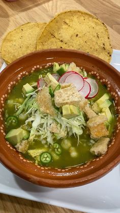 a brown bowl filled with soup next to two tortilla chips on a white plate