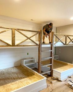 a man standing on top of a wooden bunk bed in a room with white walls