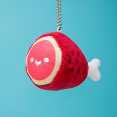 a red and white stuffed animal hanging from a silver ball chain on a blue background