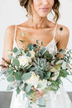 a bride holding a bouquet of flowers and greenery in her hands, wearing a wedding dress