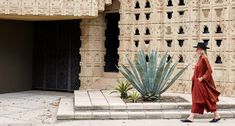 a woman walking down the street in front of a building with cactus and cacti