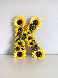 the letter k is made up of sunflowers on a white countertop with a wall in the background