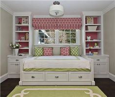 a white bed sitting under a window next to a green and white rug on top of a hard wood floor