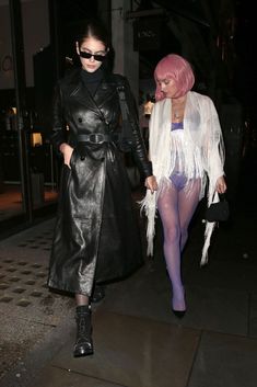 two women dressed in black and white are walking down the street at night with pink hair