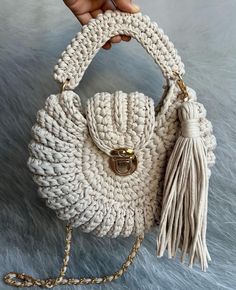 a hand holding a white crocheted purse with tassels and a chain