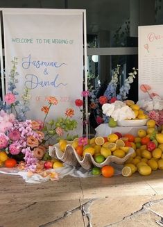 a table with flowers, lemons and oranges on it in front of a sign that says welcome to the wedding