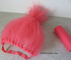 a pink tulle hat and headband laying on the floor next to a roll of toilet paper