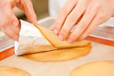 a person making cookies on top of a cookie sheet with wax paper over them and one hand holding a piece of bread