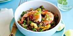 a white bowl filled with rice and shrimp on top of a blue plate next to a fork