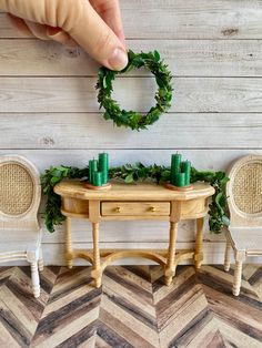 a hand reaching for candles on top of a table next to two chairs and a wreath