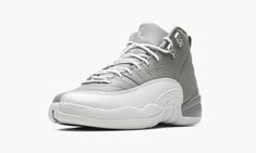 The Air Jordan 12 GS “Stealth” is the youth sizing of the retro basketball shoe in a two-tone grey and white colorway.  Originally released in 1997, the Jordan 12 was worn by Michael Jordan with the Chicago Bulls during the ‘96-97 NBA season, and in the ‘97 NBA Playoffs.  The “Stealth” honors the shoe’s 25th anniversary.  Details include a Stealth Grey tumbled leather upper paired with a white pebbled mudguard.  Metallic Silver eyelets appear on the collar, and a grey nylon pull tab is found on Gray And White Jordans, Jordan 12s, Grey Jordans, Jordan Retro 12, Retro Basketball Shoes, White Jordans, Retro Basketball, Nike Shoes Girls, Air Jordan 12