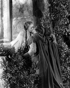 an old photo of two women dressed in medieval costumes kissing each other outside the window