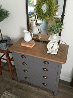 a dresser with a clock, plant and mirror on it's top shelf next to a stool