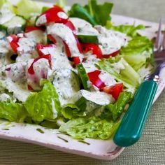 a white plate topped with lettuce and tomato salad next to a green fork