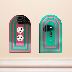 two green and pink electrical outlet covers on a beige wall, with one light switch in the middle