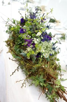 an arrangement of flowers and greenery on a white table cloth at a wedding reception