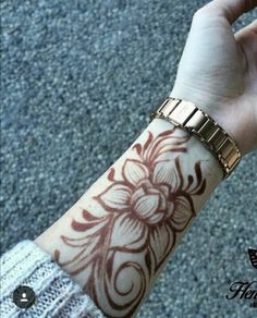 a woman's arm with a flower tattoo on it and a gold chain around the wrist