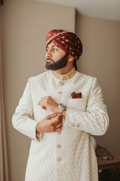 a man with a beard and turban standing in front of a mirror wearing a white suit