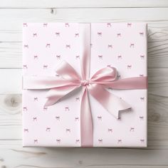 a pink wrapped present with ribbon on white wooden background, closeup view from above