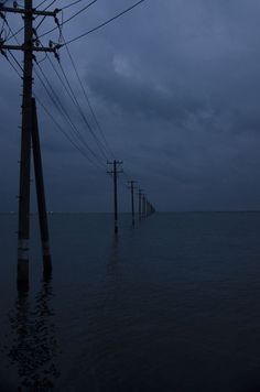 power lines and telephone poles are submerged in the ocean at night, with dark clouds overhead