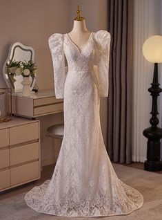 a white wedding dress on display in front of a dressing table with a mirror and lamp