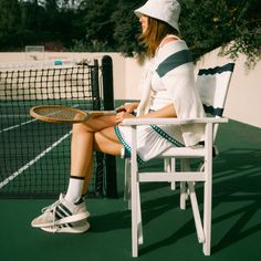 a woman sitting in a chair holding a tennis racquet on top of a tennis court