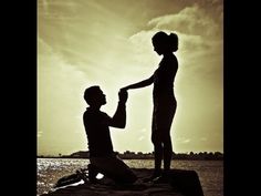 a man kneeling down next to a woman on top of a rock near the ocean