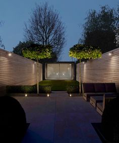 an outdoor living area at night with lights on the walls and trees in the background