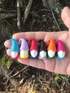 a hand is holding five small plastic gnomes in different colors and shapes, all on one finger