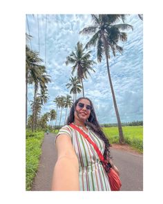 a woman taking a selfie in front of palm trees on the side of a road