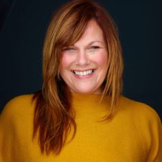 a smiling woman with red hair wearing a yellow sweater