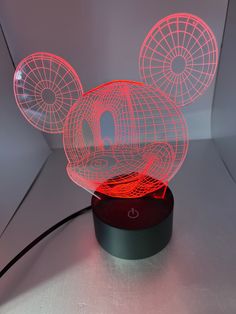 an illuminated mickey mouse head is shown on a table with a red base and black base