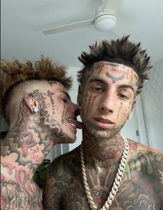 two men with tattoos and piercings on their faces, one is kissing the other