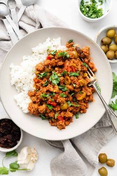 a white plate topped with meat and rice next to olives, cilantro