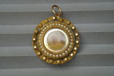 "STORY --------- Crafted in Georgian era England, this circular 15 carat gold locket is decorated with a delicate cannetille border and a row of split pearls around a glass compartment holding an old photograph.  The inner can be accessed by a hinged door to the back, decorated with blue enamel around the gold initials 'WT & SB', and surrounded by an engraved dedication reading 'In remembrance of an affectionate Mother and Father'. The photo appears to be later and has been glued within, but an Antique Medallion Jewelry With Historical Design, Victorian Medallion Jewelry With Historical Design, Victorian Medallion With Historical Design Jewelry, Gold Medallion Jewelry With Historical Design, Historical Medallion Jewelry For Weddings, Historical Medallion Design Jewelry For Wedding, Medallion Jewelry With Historical Design For Weddings, Historical Round Jewelry For Weddings, Victorian Round Pendant Wedding Jewelry