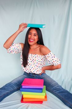 a woman sitting on the floor holding a stack of colorful folders over her head