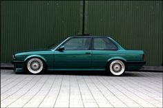 a green car parked in front of a building with white rims on it's tires