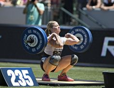 a woman squats on the ground with a barbell in front of her and another person behind her