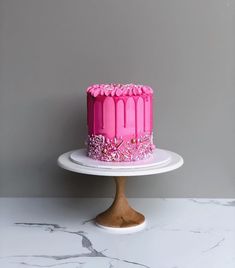 a pink cake sitting on top of a white cake plate next to a gray wall