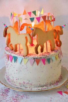 a birthday cake decorated with horses and bunting streamers on a white tablecloth