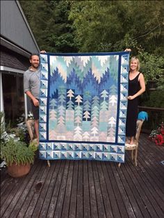 two people holding up a blue and white quilt on a wooden deck with potted plants