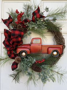 an old red truck is adorned with pine cones, berries and greenery to create a christmas wreath