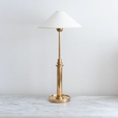 a white lamp sitting on top of a marble counter next to a light fixture with a gold base