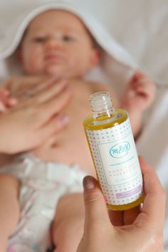 a woman holding a bottle of baby oil in front of a baby's face