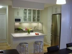 a kitchen with white cabinets and stainless steel appliances in the center, along with bar stools