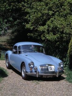 an old blue car parked on the side of a road next to some bushes and trees