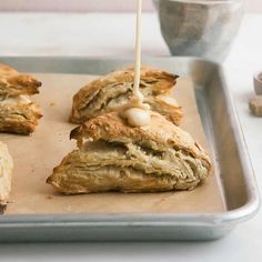 some food that is sitting on a baking sheet and being drizzled with white sauce