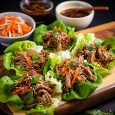 lettuce wraps with shredded meat and carrots on a cutting board next to bowls of dipping sauce